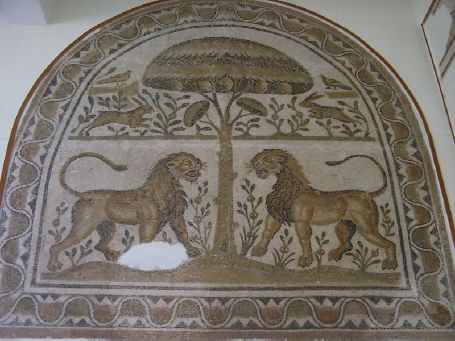 Mosaico d'abside dove, dentro un quadrato delimitato da un nastro che riproduce dei fiori di loto, si vede una decorazione che si sviluppa su due registri: in primo piano due leoni di affrontano di fronte a un pino; in secondo piano due lepri si oppongono davanti allo stesso albero